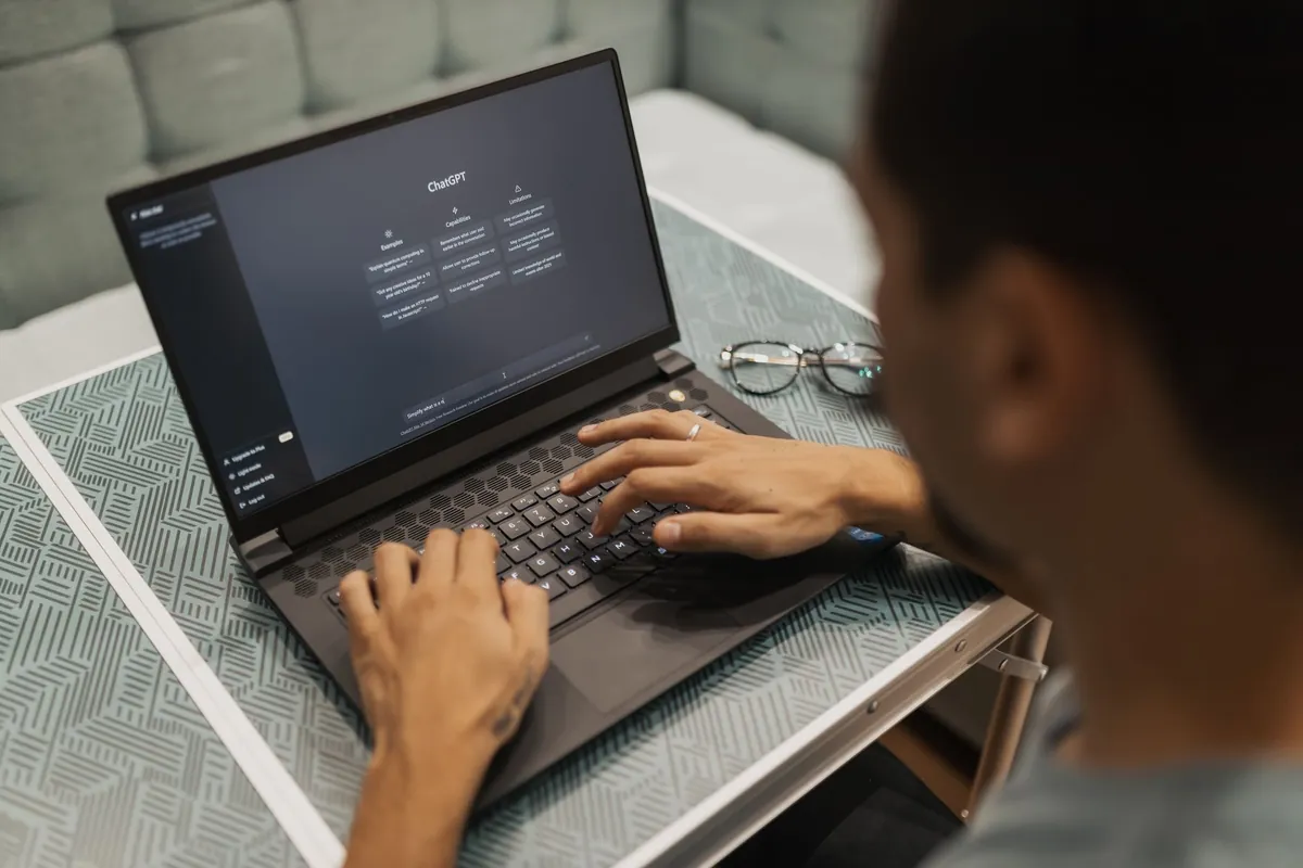 Pessoa digitando num notebook com a tela inicial de um assistente de IA aberta