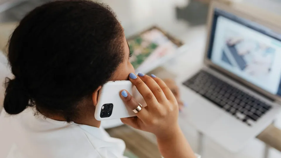 Recepcionista de clínica atendendo ao telefone com um computador à frente