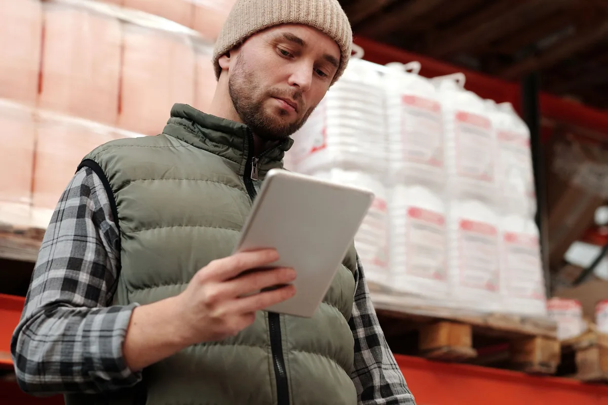 Funcionário de armazém conferindo o estoque em um tablet, entre prateleiras de um galpão industrial
