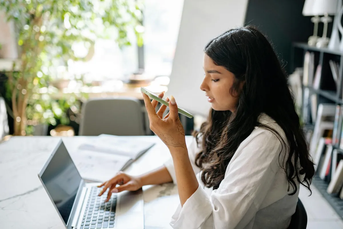 Mulher em escritório claro falando ao celular enquanto digita no notebook