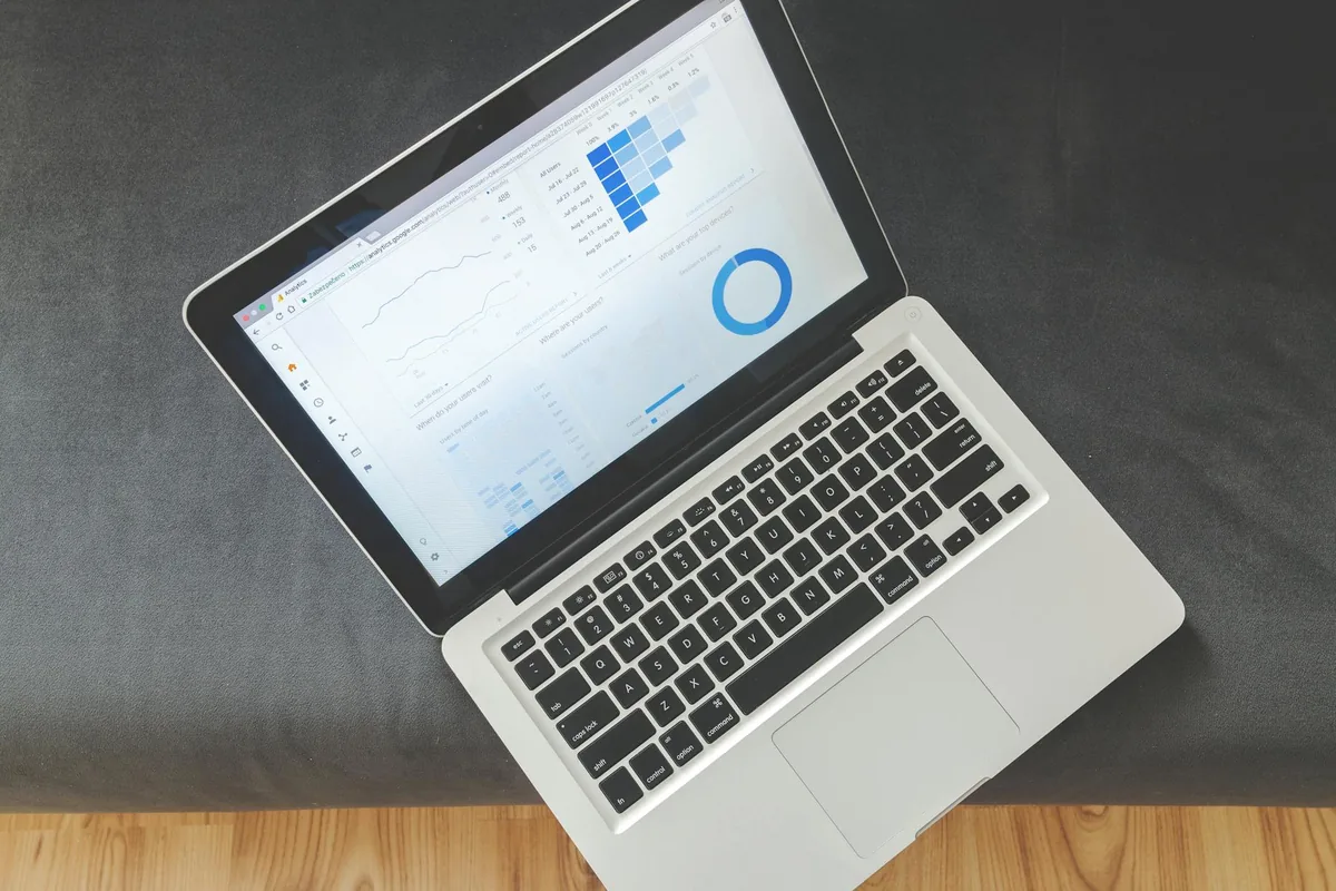 Laptop aberto sobre mesa de trabalho, visto de cima, exibindo planilhas e gráficos